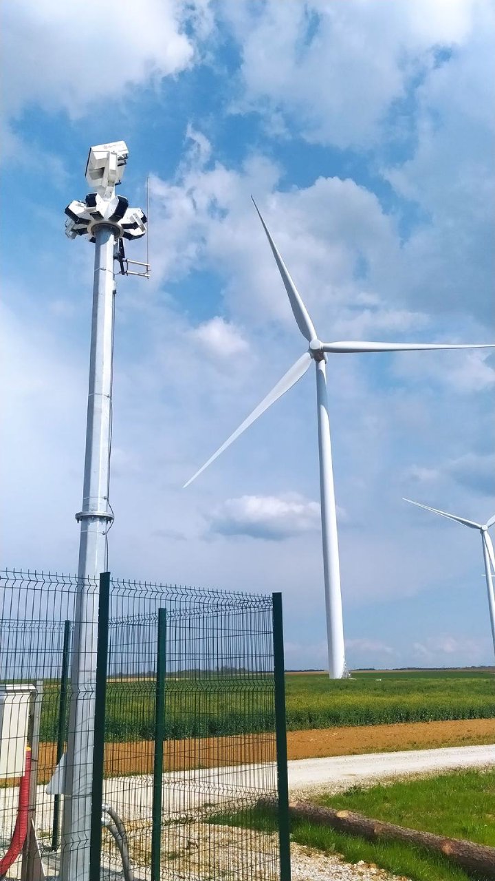Bird detection camera on a mast next to a wind turbine